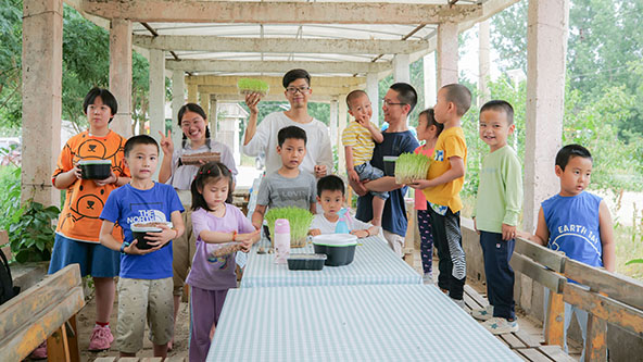 Young children holding plants and two adults standing around a table
