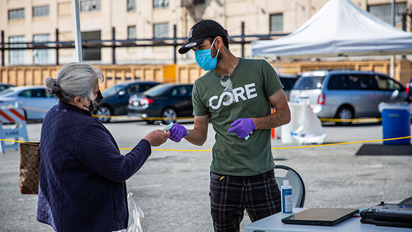 A man wearing a mask and surgical gloves hands a woman a slip of paper at a mobile COVID-19 vaccination site in Los Angeles, California.