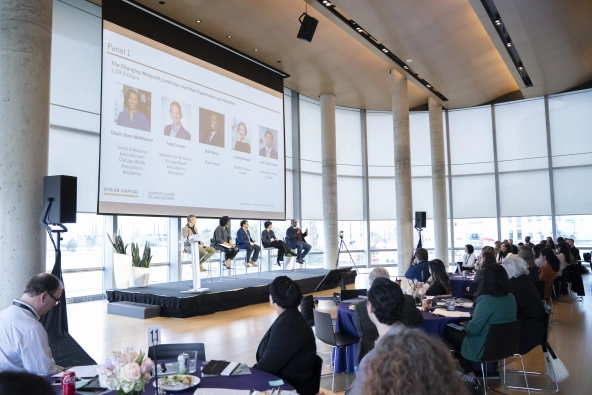 five people sitting on a stage for a panel discussion with an audience