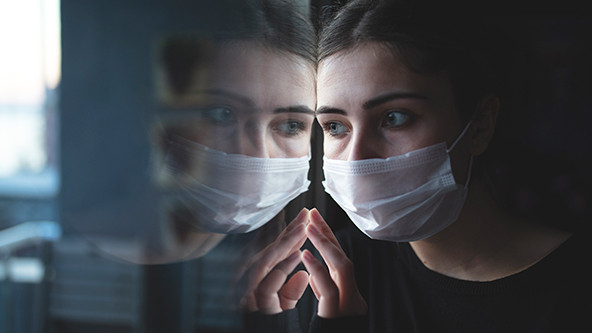 Woman wearing a surgical mask and staring out a window.