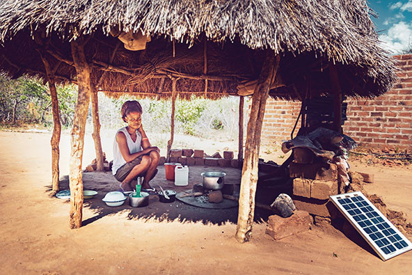 A young women cooking corn maze under a hut with a solar-powered stove
