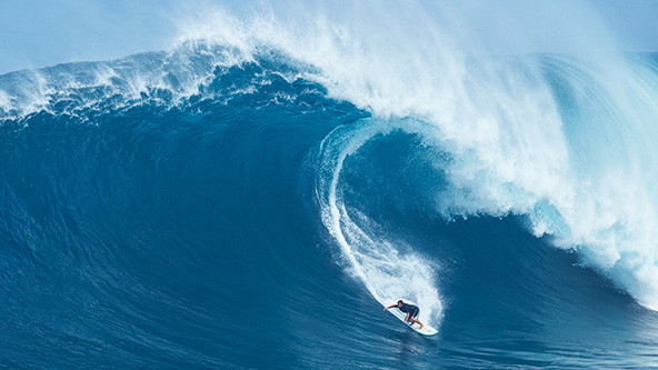 Man on a surfboard under a giant wave