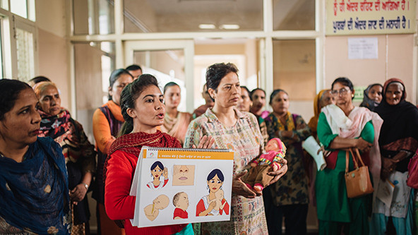 A nurse holding a flipchart trains family members how to care for newborns