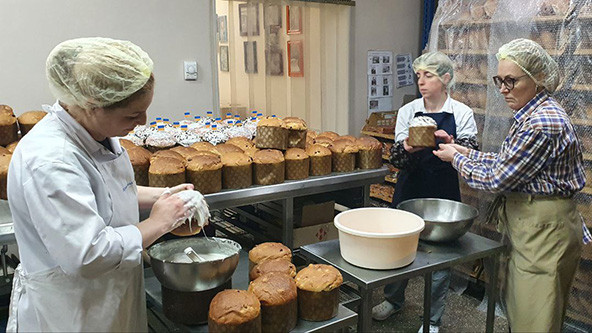 Three people in a commercial kitchen baking bread and putting frosting on bread.