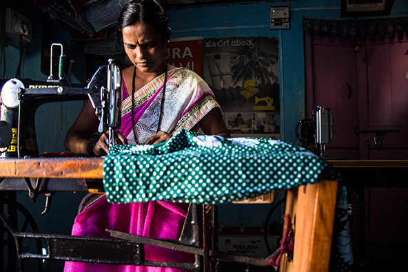 A woman in India using a solar-powered sewing machine under solar-powered lighting