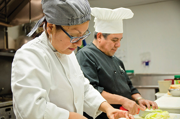 Two people in chef's coats cutting vegetables