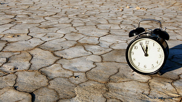 Alarm clock reading 5 minutes til 12 sitting on dry, cracked ground