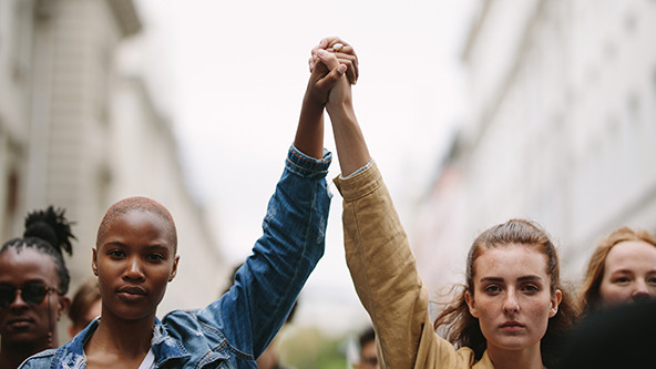 Two activists, one Black woman and one white woman, holding raised hands.