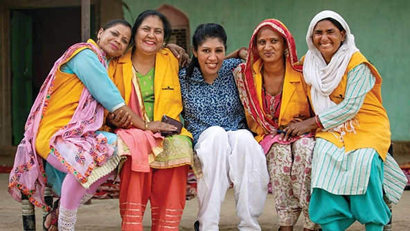 five women wearing brightly colored saris sitting for a photo