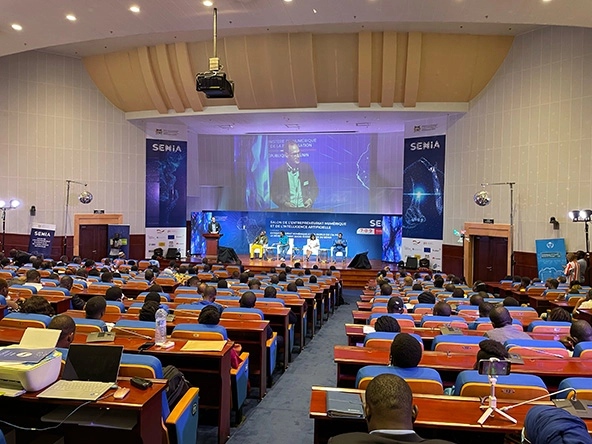 Panelists on a stage in a large room with people seated in rows in the crowd