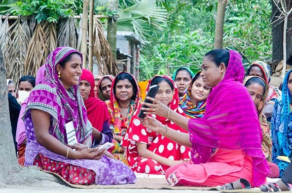 A woman holds up a digital tablet to show another woman something on the screen.