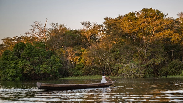 young girl rowing a traditional wooden boat along the Amazon River at sunset in Brazil