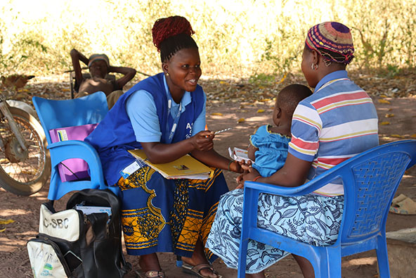 community health worker sits and talks with a mother holding her child