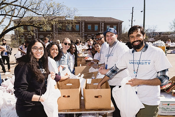 Diverse group of college students standing at a table with boxes facing camera and smiling