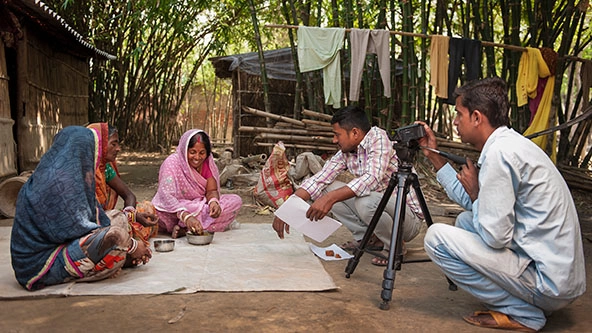 Videographer crouching on the ground filming a community video for the NGO Digital Green