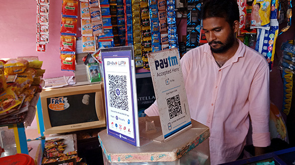 Indian man in a market; signs with QR codes to use for payment