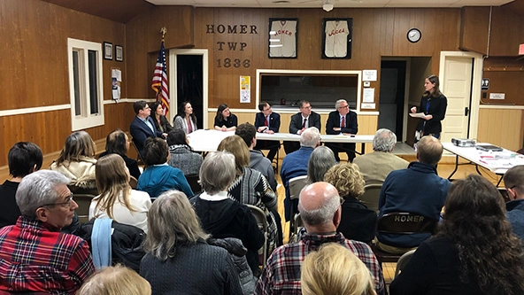 People sitting at a head table with an audience of people in chairs.