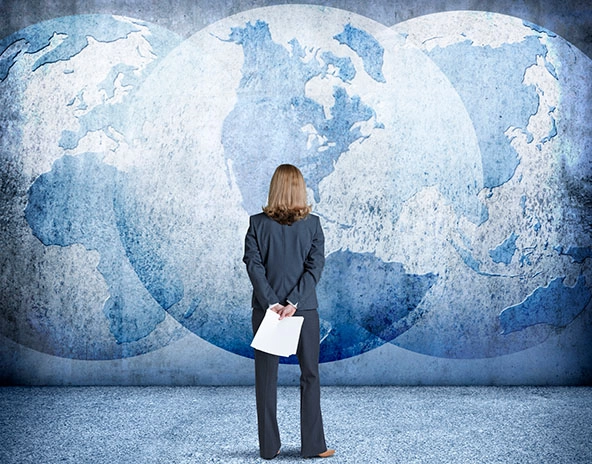 Businesswoman looks up at three interlocking globes on a wall