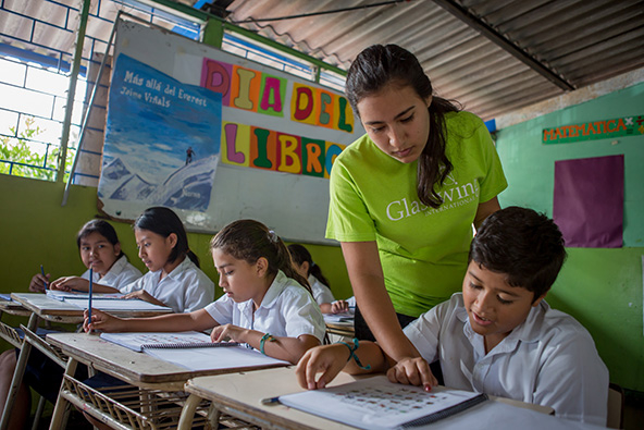 A teacher helps a young student sitting at a school desk