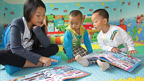 A young woman reads with two toddlers in a colorful room at a parenting center in Souther Shaanxi Province, China.