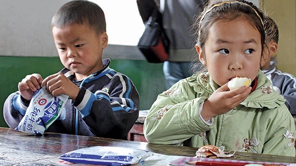 Two children sitting at a table and eating hard-boiled eggs.