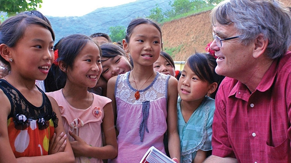 A man in a red shirt speaks with young school children.