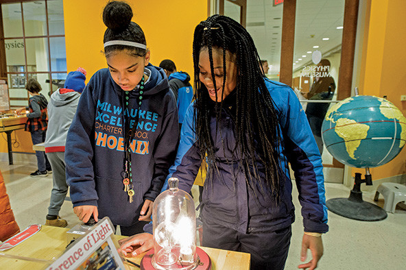 Two students stand with a large glowing light bulb at a hands-on exhibit about electricity.