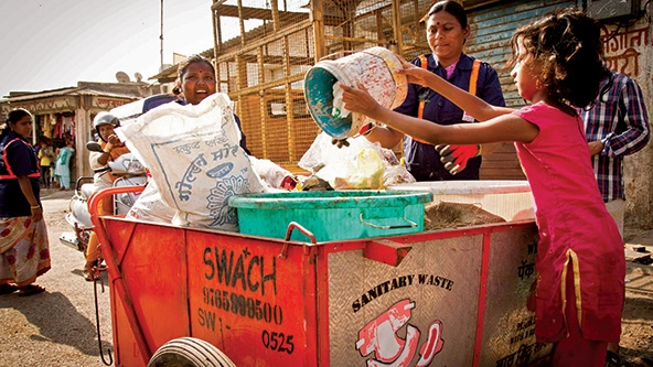 Workers dumping sanitary waste into a pushcart that says SWaCH, sanitary waste.