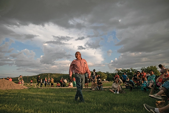 A First Nations man talking to a crowd of people in a field