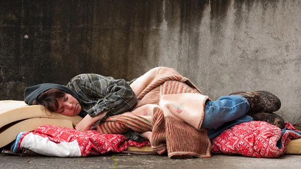 Homeless woman sleeping with blankets and a foam mattress on the street