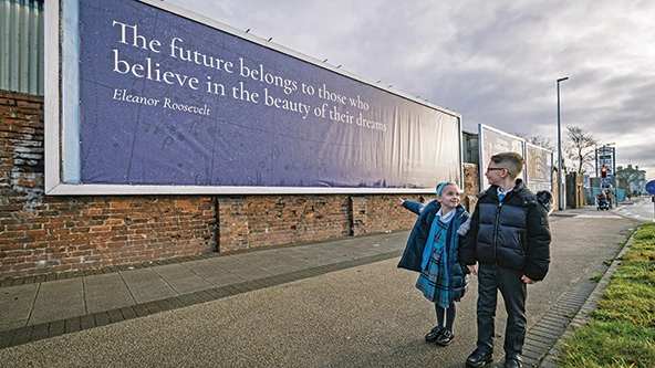 Two children look at a billboard with a quote from Eleanor Roosevelt that reads, 