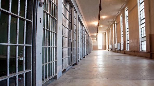 Hallway inside the Old Idaho State Penitentiary with prison cells on the left and windows on the right.