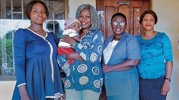 Woman holding an infant stands with three other women in front of building
