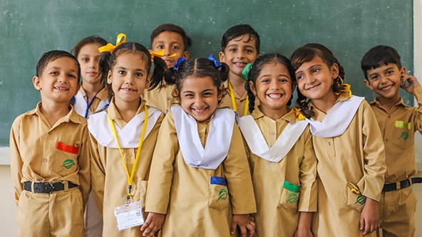 Young school students standing together with chalkboard behind them.
