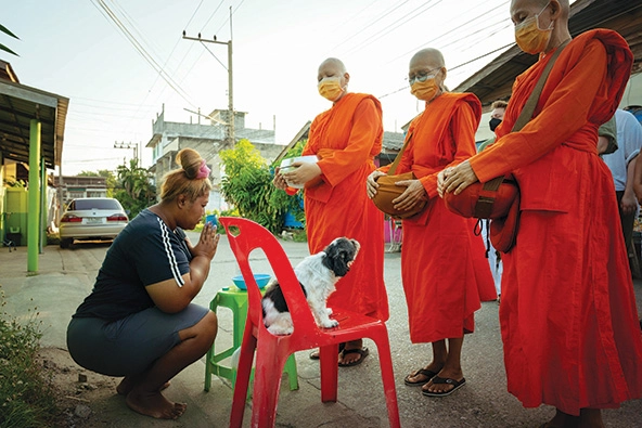 woman kneels next to her dog as three female buddhist monks bless her and her dog