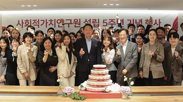 Group of people in business attire stand behind a cake