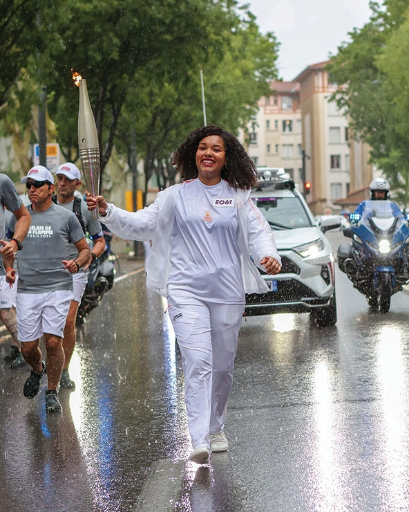 Woman in white track suit running in the rain holding the Olympic torch