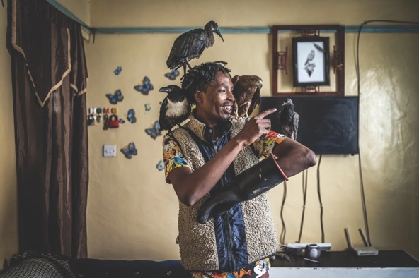smiling man in a room with birds perched on his body