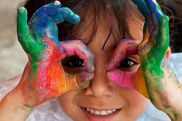 child with painted hands making binoculars with thumb and forefinger; facing camera