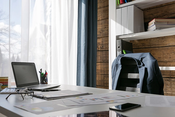 desk with laptop and empty chair with suit jacket hanging on the back