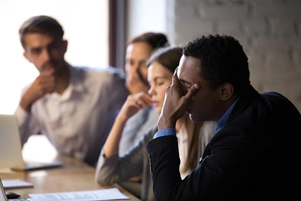 Employees sit at a table with head in hands