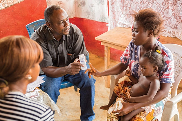 Man showing a bottle of medication to a mother with child in lap