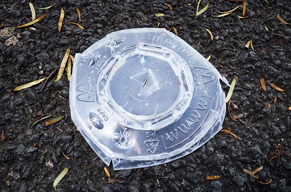 A crumpled plastic McDonald's soda lid lays on the ground