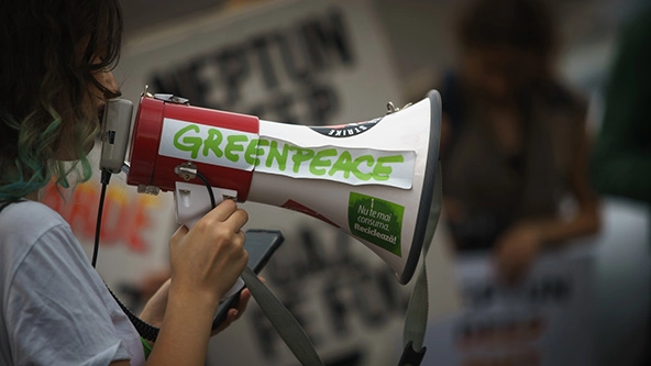 An activist shouts into a bullhorn with a Greenpeace sticker on the side