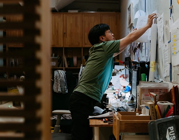 Man reaching over a table to arrange papers on a wall