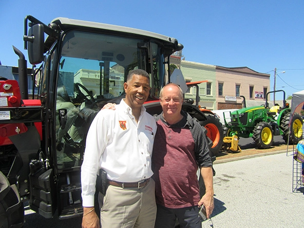 Two men with arms on each others shoulders standing in front of a tractor 