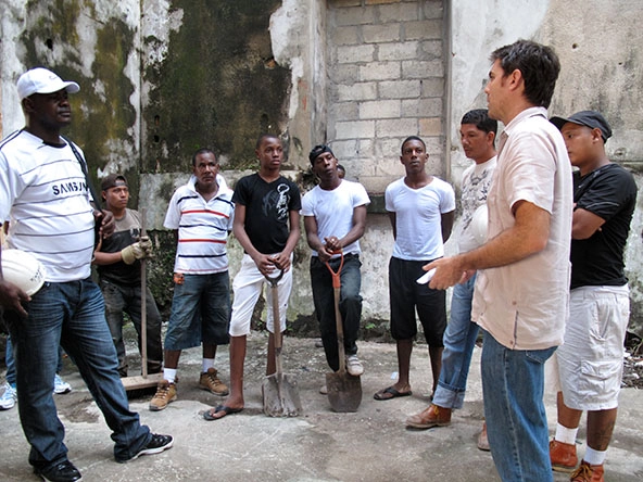 Men standing in a semi-circle listening to one may talk.