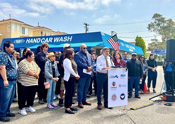 group of people standing around a podium in front of a carwash, american flag