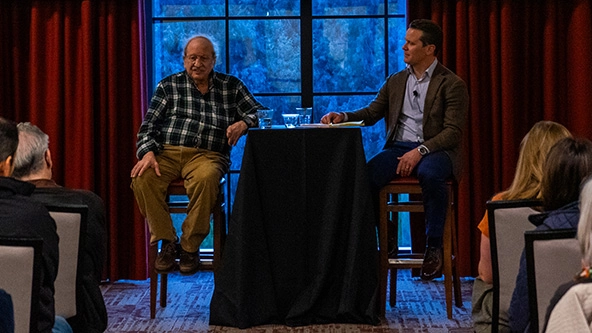 two men sitting at a table in front of a crowd