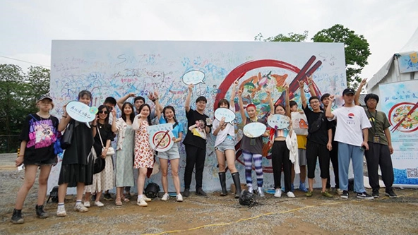 People standing outside in front of a sign with a bowl of food and chopsticks painted on it
